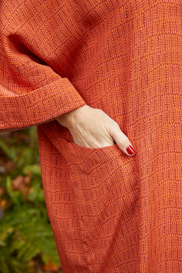 Close up of sleeve, pocket and woman's hand in pocket of Dessous Loungewear Bianca caftan in orange and red print sustainable Lyocell fabric.