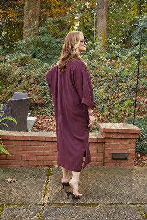 Back view of blonde woman wearing Dessous Loungewear Bianca caftan in plum colored sustainable Lyocell fabric.