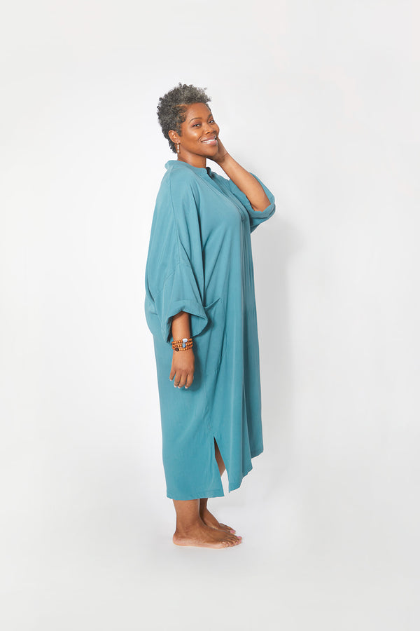 Side view of beautiful black woman wearing Dessous Loungewear's Bianca caftan midi dress in sustainable Lyocell turquoise fabric.