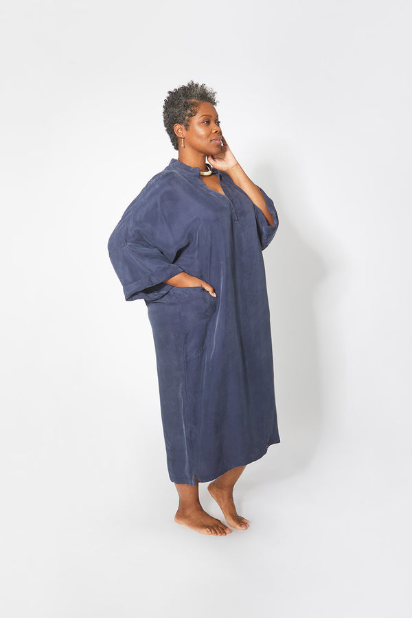 Side view of beautiful black woman wearing Dessous Loungewear Bianca caftan in navy sustainable Cupro fabric. Caftan with pockets.