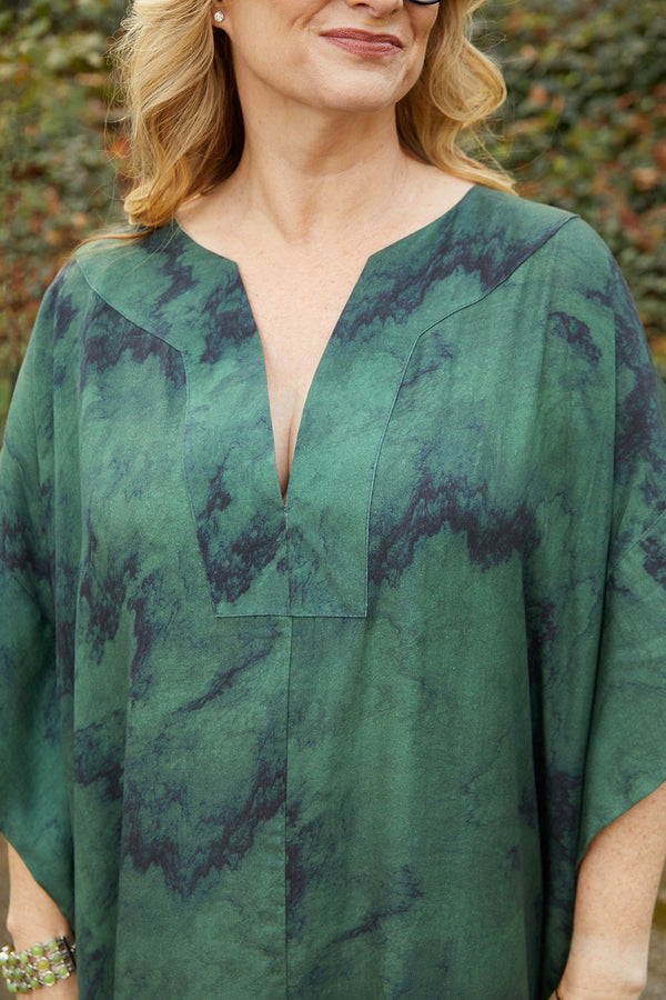 Close-up photo of a woman wearing a green and navy marble print caftan in eco-friendly Tencel Lyocell fabric. The caftan is maxi-length with a V neckline.