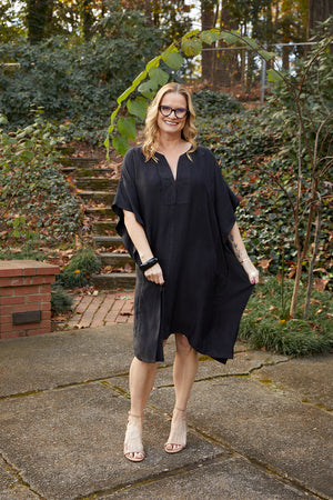 Woman outdoors wearing Dessous Loungewear's new knee-length eco-friendly Grace caftan in black Cupro blend fabric. Cupro is made from the waste fibers left behind from cotton processing. It is breathable, sustainable and feels like washable silk.